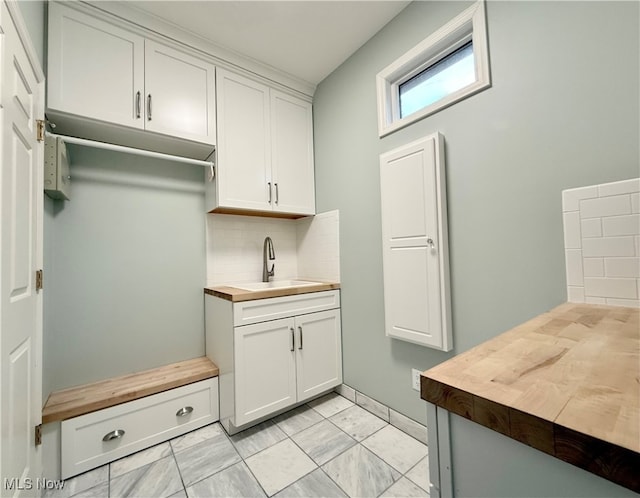 interior space with decorative backsplash, butcher block countertops, white cabinetry, and sink