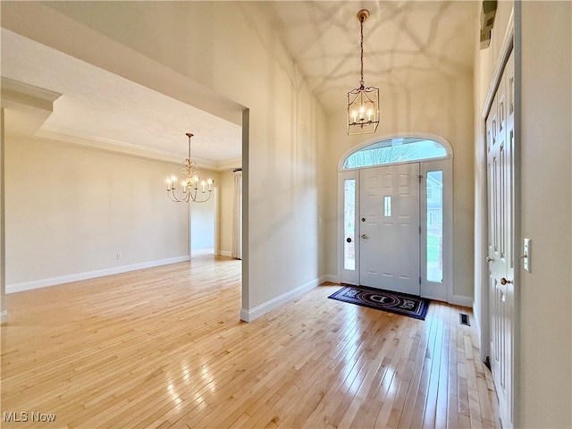 entryway featuring a towering ceiling, light wood-type flooring, an inviting chandelier, and ornamental molding