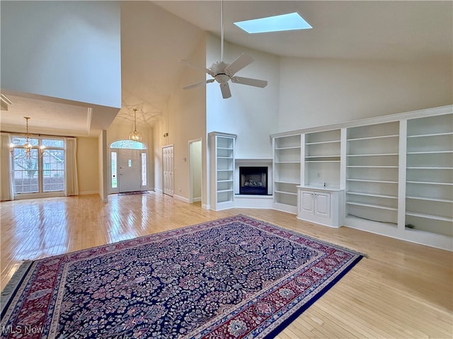 unfurnished living room with a skylight, high vaulted ceiling, wood-type flooring, and ceiling fan with notable chandelier