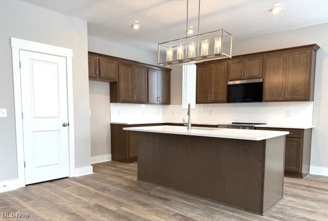 kitchen with pendant lighting, hardwood / wood-style floors, a kitchen island with sink, and tasteful backsplash