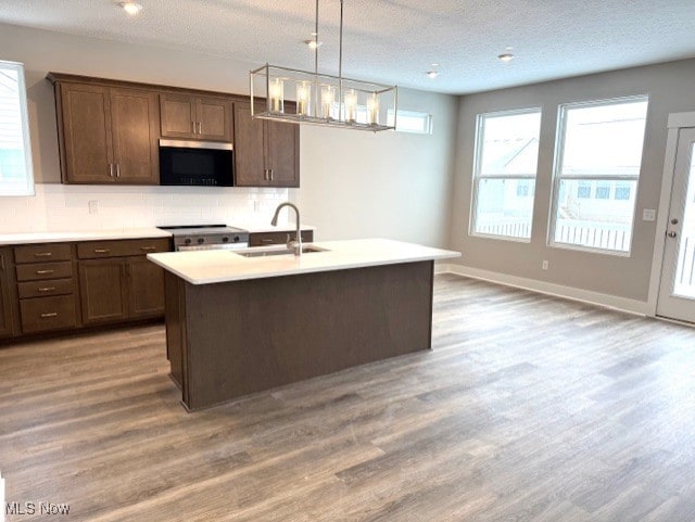 kitchen with dark brown cabinetry, sink, range, hanging light fixtures, and decorative backsplash