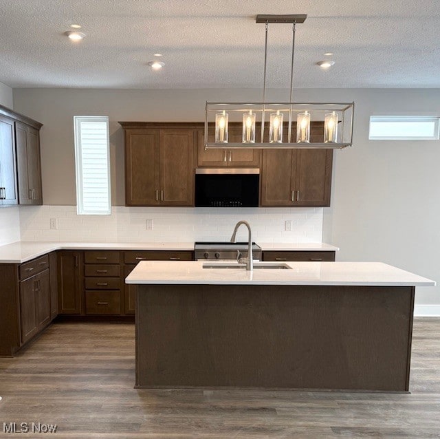 kitchen featuring a kitchen island with sink, hanging light fixtures, dark brown cabinetry, and sink