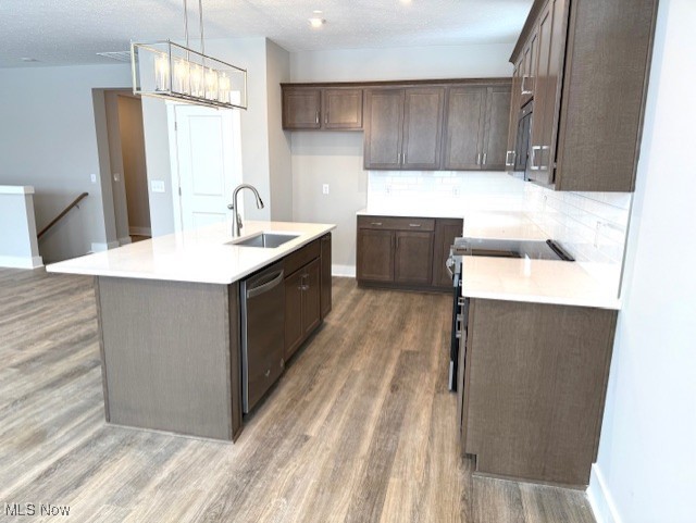 kitchen featuring dark hardwood / wood-style floors, decorative light fixtures, an island with sink, sink, and stainless steel appliances