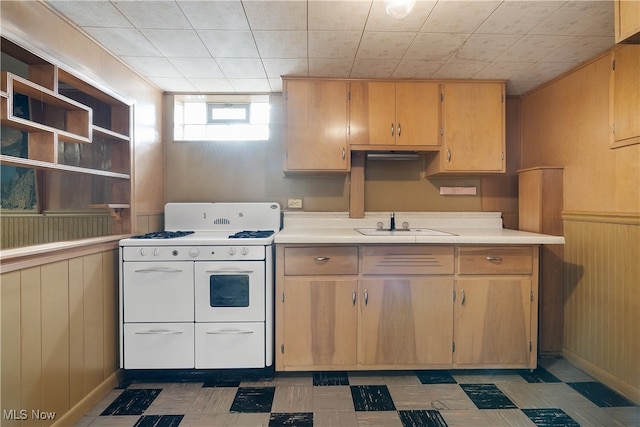 kitchen with wood walls, light brown cabinets, and white range with gas stovetop