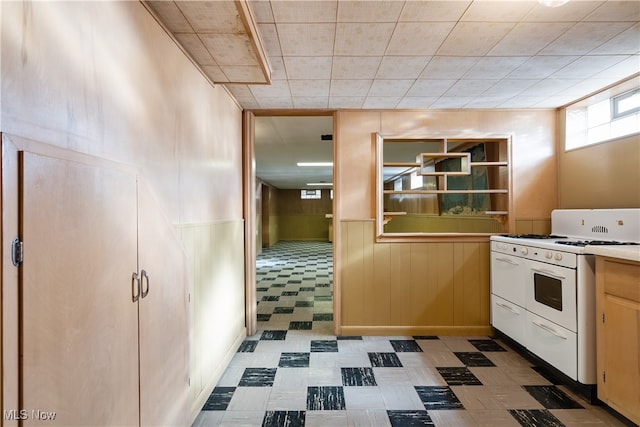 kitchen featuring white gas range oven and wood walls