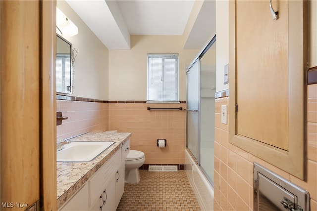 full bathroom with tile patterned flooring, enclosed tub / shower combo, toilet, vanity, and tile walls