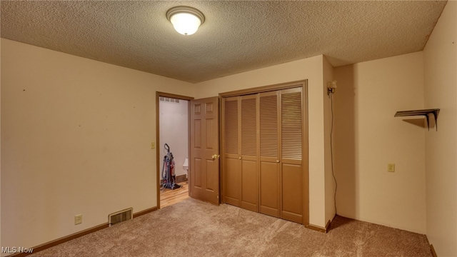 unfurnished bedroom featuring a textured ceiling, light colored carpet, and a closet