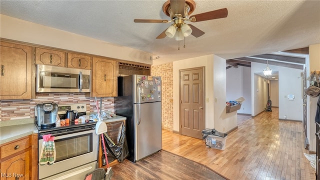 kitchen featuring hanging light fixtures, stainless steel appliances, a textured ceiling, decorative backsplash, and light wood-type flooring