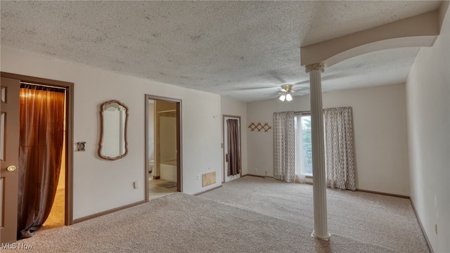 unfurnished room with a textured ceiling, light colored carpet, ceiling fan, and decorative columns