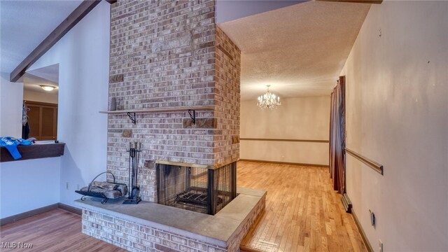 living room featuring a brick fireplace, a notable chandelier, light hardwood / wood-style floors, a textured ceiling, and lofted ceiling