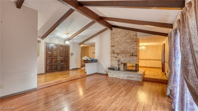 unfurnished living room featuring a chandelier, vaulted ceiling with beams, hardwood / wood-style flooring, and a brick fireplace