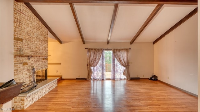 unfurnished living room with a fireplace, lofted ceiling with beams, and light hardwood / wood-style floors