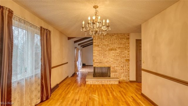 unfurnished dining area featuring a brick fireplace, an inviting chandelier, light hardwood / wood-style flooring, a textured ceiling, and lofted ceiling