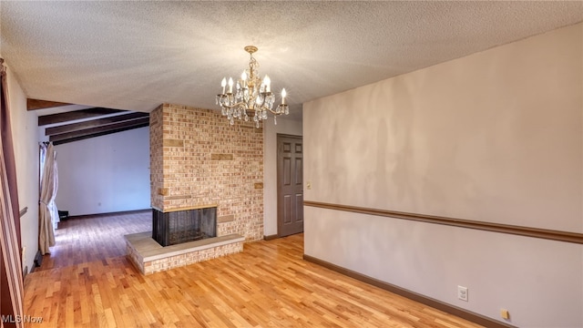 unfurnished living room with a chandelier, a textured ceiling, light wood-type flooring, and a brick fireplace