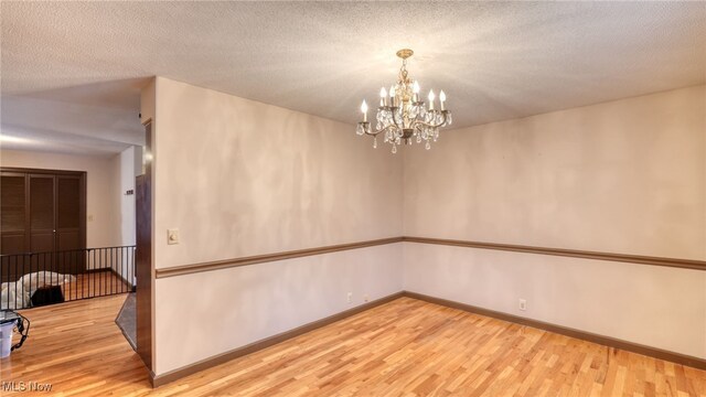 unfurnished room featuring a chandelier, a textured ceiling, and hardwood / wood-style flooring