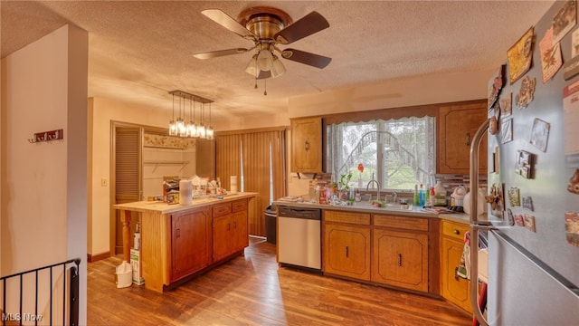 kitchen with appliances with stainless steel finishes, sink, wood-type flooring, a kitchen island, and hanging light fixtures