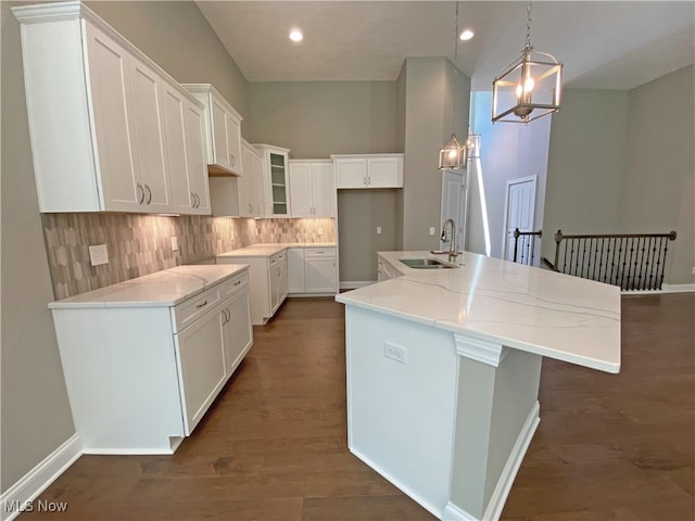 kitchen featuring white cabinetry, sink, dark wood-type flooring, an island with sink, and decorative light fixtures