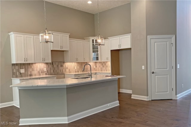 kitchen with high vaulted ceiling, white cabinets, sink, an island with sink, and a textured ceiling