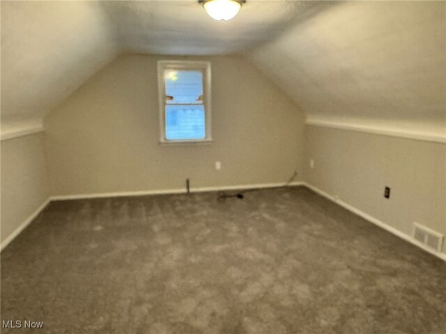 additional living space featuring lofted ceiling and dark colored carpet