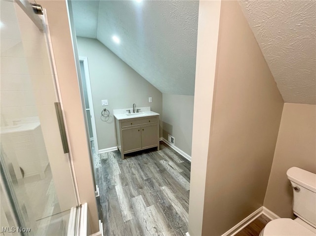 bathroom featuring vanity, a textured ceiling, vaulted ceiling, wood-type flooring, and toilet