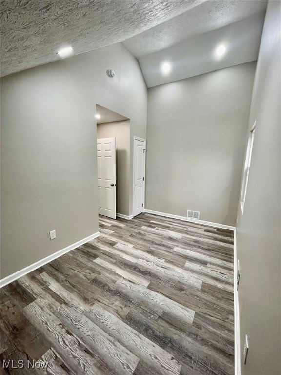 unfurnished room with high vaulted ceiling, a textured ceiling, and hardwood / wood-style flooring