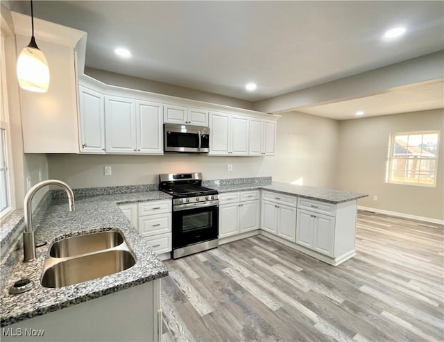 kitchen with kitchen peninsula, appliances with stainless steel finishes, sink, white cabinetry, and hanging light fixtures