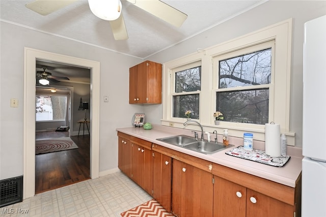 kitchen with a textured ceiling, ceiling fan, sink, white fridge, and light hardwood / wood-style floors