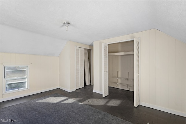 bonus room featuring a textured ceiling, wood walls, dark hardwood / wood-style floors, and lofted ceiling