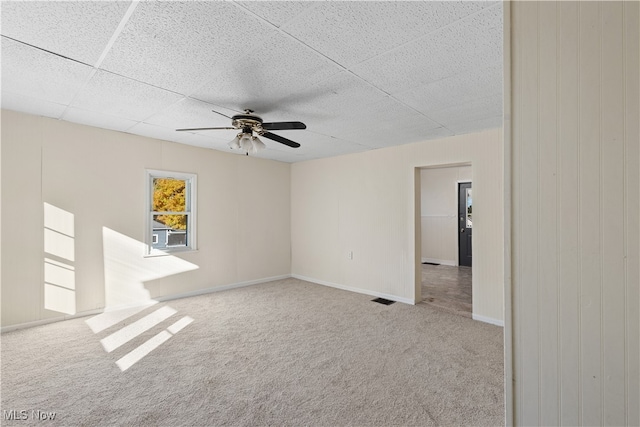 carpeted empty room with ceiling fan and a drop ceiling