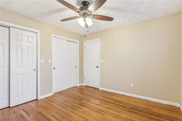 unfurnished bedroom featuring wood-type flooring, ceiling fan, and multiple closets