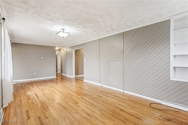 spare room with built in shelves, wood-type flooring, and wooden walls