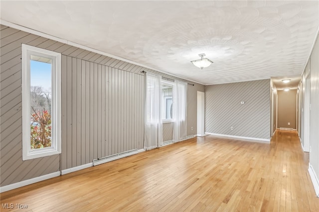 interior space with baseboard heating, wood walls, and light hardwood / wood-style floors