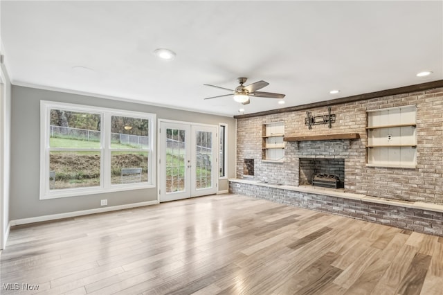 unfurnished living room featuring ceiling fan, light hardwood / wood-style flooring, brick wall, and a brick fireplace