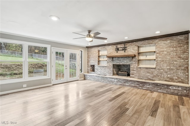 unfurnished living room featuring french doors, a brick fireplace, brick wall, ceiling fan, and light hardwood / wood-style floors