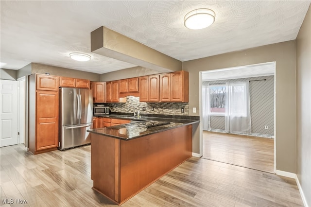 kitchen with light wood-type flooring, kitchen peninsula, appliances with stainless steel finishes, and dark stone counters