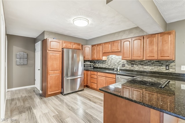 kitchen with kitchen peninsula, appliances with stainless steel finishes, dark stone counters, sink, and light hardwood / wood-style flooring