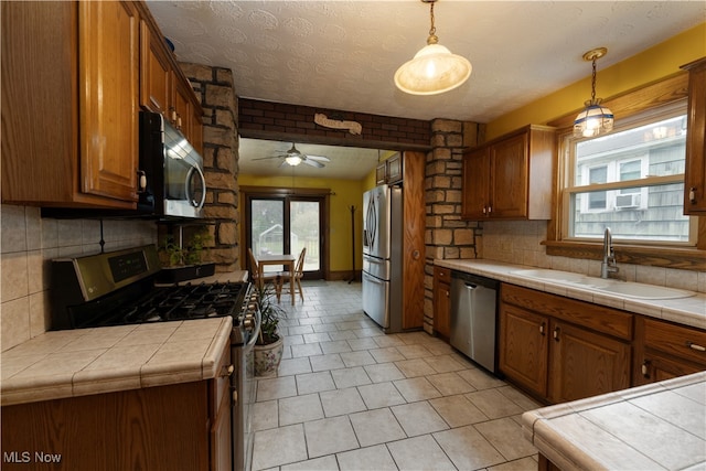 kitchen featuring tasteful backsplash, tile counters, brown cabinets, appliances with stainless steel finishes, and a sink