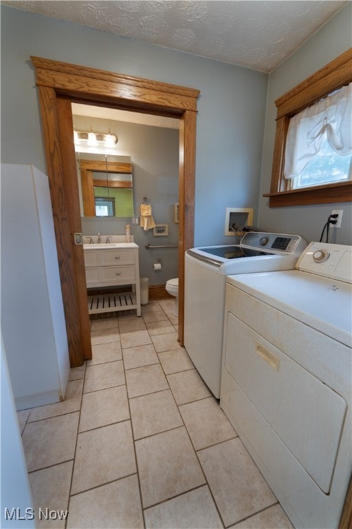 laundry area with washer and dryer, a sink, a textured ceiling, light tile patterned flooring, and laundry area