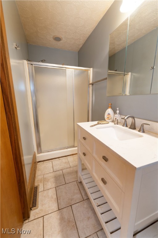 bathroom featuring vanity, visible vents, tile patterned flooring, a shower stall, and a textured ceiling