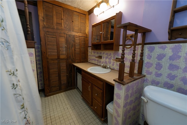 bathroom featuring a textured ceiling, vanity, toilet, and tile walls