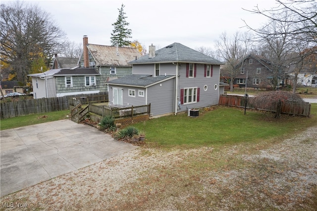 rear view of house featuring a yard, fence, cooling unit, and a shingled roof