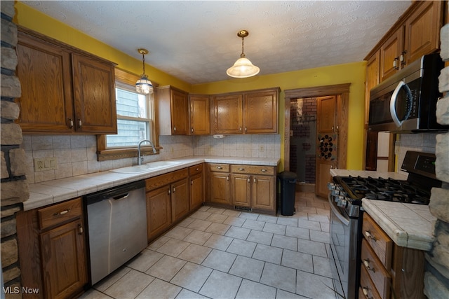 kitchen featuring tile countertops, stainless steel appliances, brown cabinets, and a sink