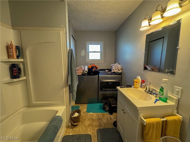 bathroom featuring vanity, a textured ceiling, separate washer and dryer, tile patterned flooring, and a tub