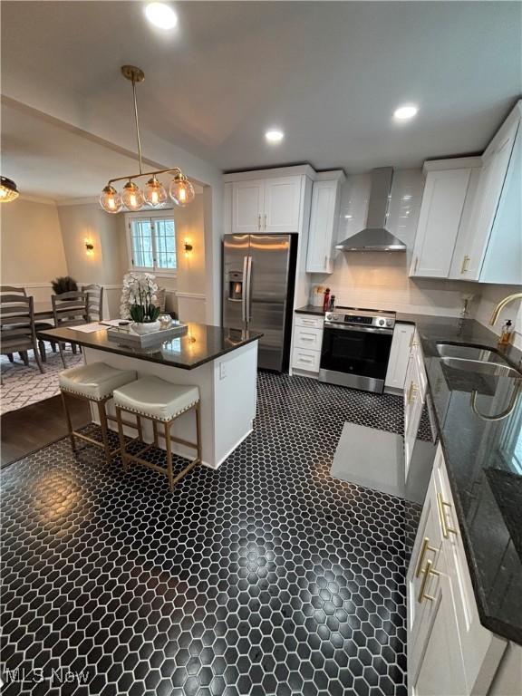 kitchen with hanging light fixtures, appliances with stainless steel finishes, white cabinetry, and wall chimney exhaust hood