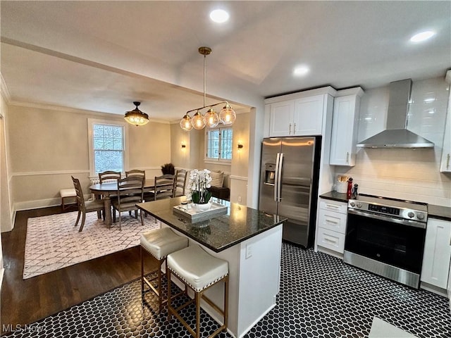 kitchen with a breakfast bar area, stainless steel appliances, white cabinets, wall chimney range hood, and pendant lighting