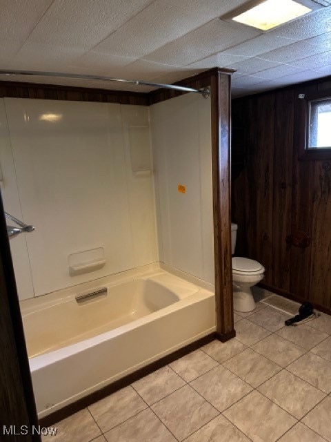 bathroom with tile patterned flooring, toilet, shower / washtub combination, and wood walls