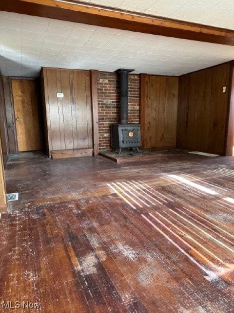 unfurnished living room with a wood stove, wooden walls, dark hardwood / wood-style flooring, and beamed ceiling