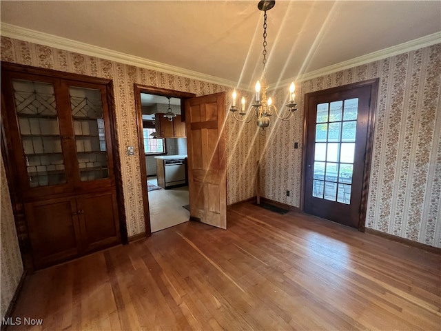 unfurnished dining area with hardwood / wood-style floors, ornamental molding, and a notable chandelier