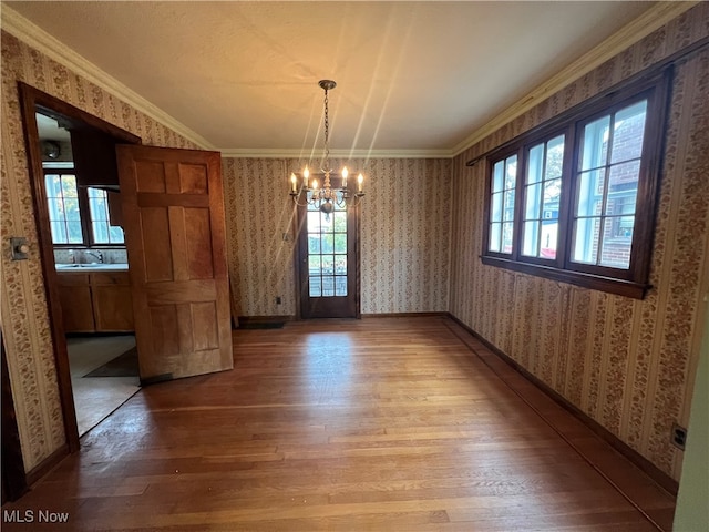 unfurnished dining area with a healthy amount of sunlight, wood-type flooring, crown molding, and an inviting chandelier