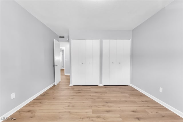 unfurnished bedroom with two closets and light hardwood / wood-style flooring